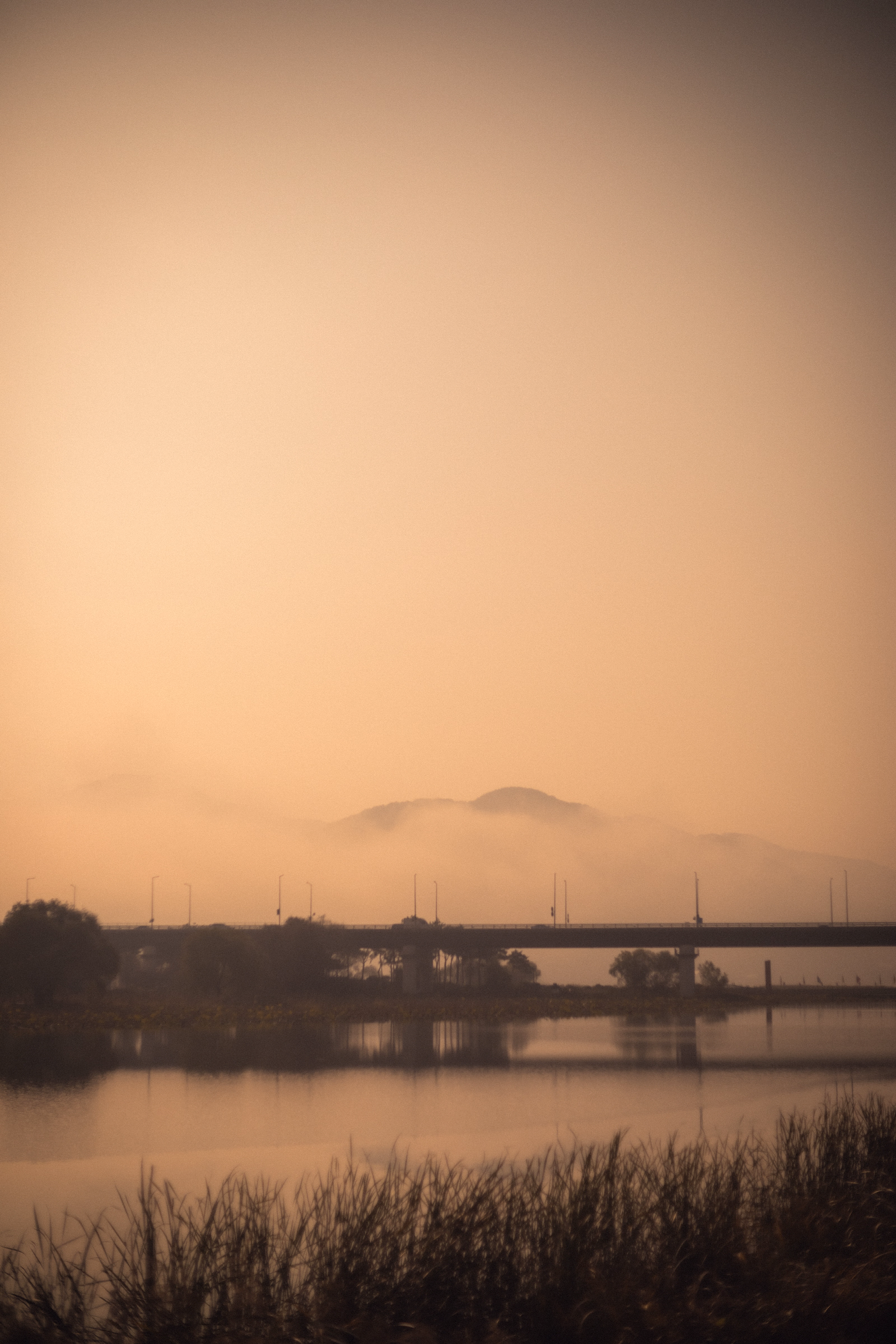 Misty Bridge Over Calm River At Foggy Sunrise With Mountain Silhouette